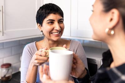 Two women standing together in a kitchen smiling and holding coffee mugs